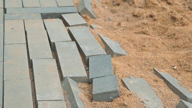 damaged pathway where stones are unevenly placed on a sandy surface. The area shows construction activity with loose stones and disturbed ground