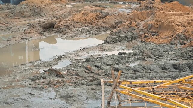 Heavy rainfall has created large puddles and muddy conditions on a construction site. Workers navigate the wet ground as they manage their tasks
