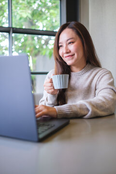 Vertical portrait image of a woman drinking coffee while working on laptop computer
