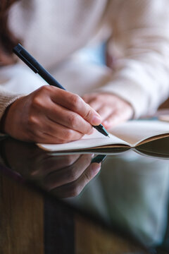 Vertical closeup image of a woman writing on a notebook on the table