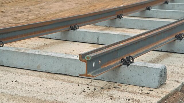 installing railway tracks by placing concrete sleepers on a prepared surface. The process includes aligning the tracks and securing them for stability