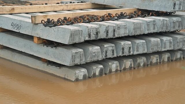 Concrete blocks are stacked on wooden pallets by the edge of water. The storage area supports various construction activities and showcases the material used in building projects