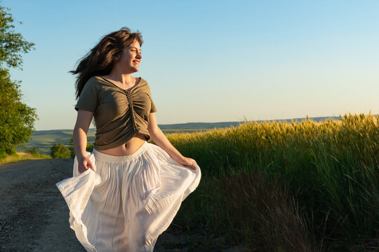 Happy young woman dancing in white skirt on country road during golden hour