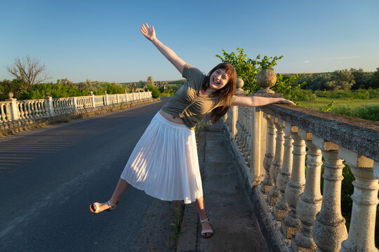 Happy young woman dancing and celebrating on a bridge railing at sunset
