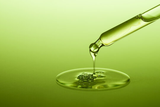 Dropperwith a drop of cosmetic serum or gel spread on green background.
