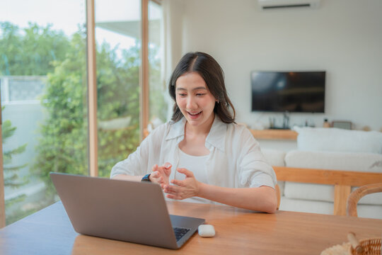 Young Asian woman presenting ideas during virtual meeting on laptop, remote worker communicating with team from bright living room.