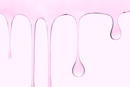Transparent cosmetic gel dripping down on pink background.