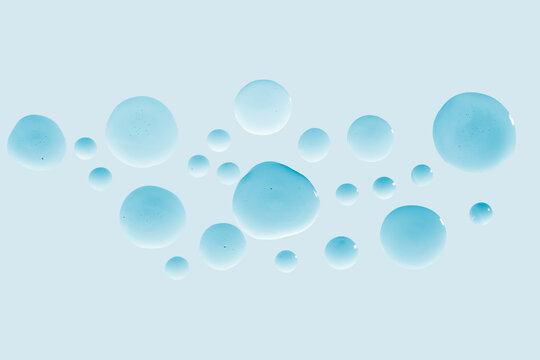 Clear cosmetic gel or face serum drops on blue background.