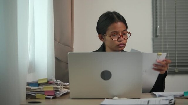 Young Businesswoman Reviewing Documents While Working on Laptop in Modern Office