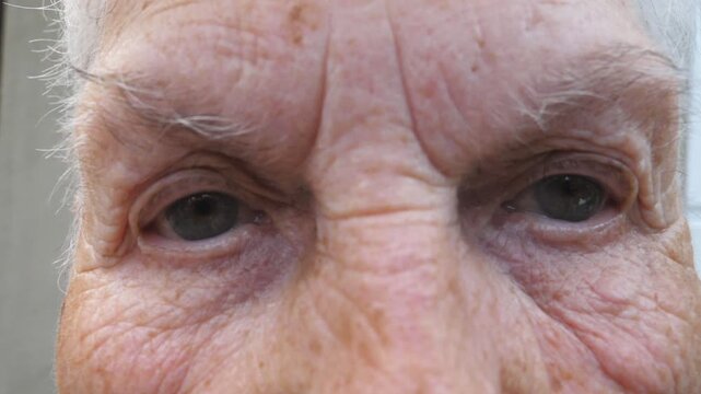 Close up gray eyes of elderly woman with wrinkles around them. Portrait of grandmother looking into camera with a sad sight. Sorrow facial expression of senior lady