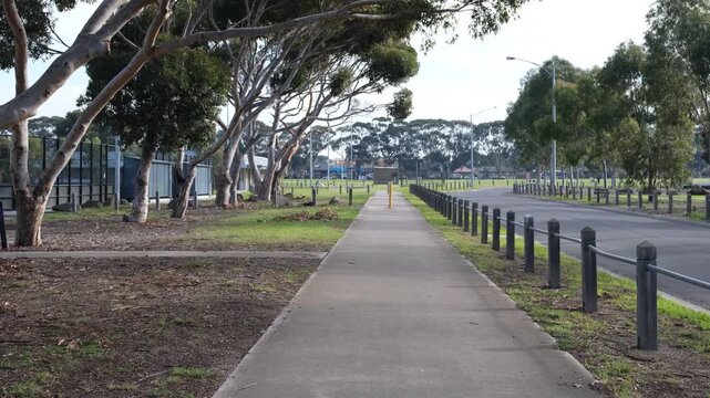 A footpath beside a bollard-lined road under gum trees, showcasing typical Melbourne public park amenities. Community infrastructure, and everyday outdoor recreation in Australian suburbs.