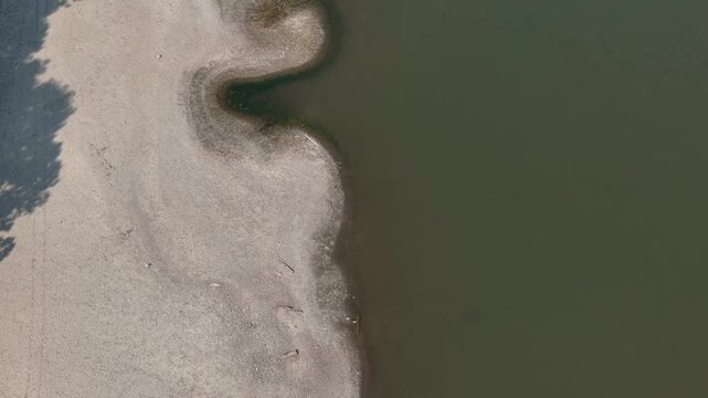 Po River suffering from critical water levels and extensive drying, revealing a broad, exposed riverbed and multiple boats resting on the dry ground near the cities of Cremona and Piacenza