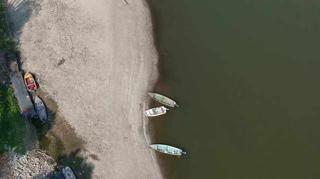 Po River suffering from critical water levels and extensive drying, revealing a broad, exposed riverbed and multiple boats resting on the dry ground near the cities of Cremona and Piacenza