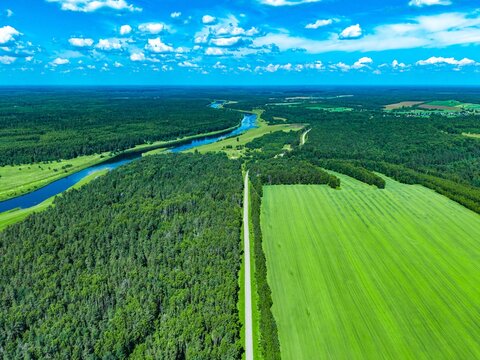 Lush green fields and winding river under bright blue sky captured from above in expansive landscape