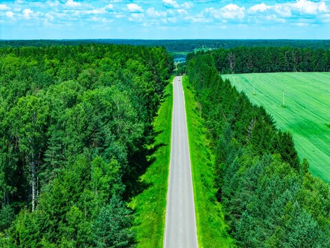 Aerial view showcasing a long winding road bordered by lush green forests and fields
