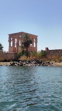 Point of view from a boat navigating the nile river and approaching the historic Trajan temple in philae temple complex with the kiosk of trajan