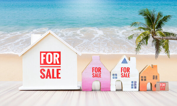 Wooden house model will for sale sign over tropical beach background, real estate business