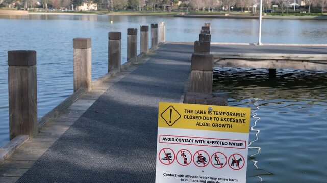 A public warning sign at a lake reads, "THE LAKE IS TEMPORARILY CLOSED DUE TO EXCESSIVE ALGAL GROWTH. AVOID CONTACT WITH AFFECTED WATER," and warning prohibiting activities in Melbourne Australia