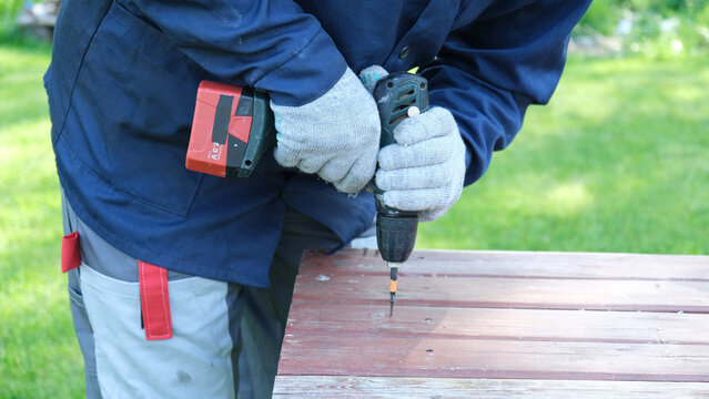 Worker man working with Screwdriver. Person using a red cordless drill with a metal spiral drill bit in a workshop, construction, diy project task. Accu battery hand drill. Screwing a screw assembling