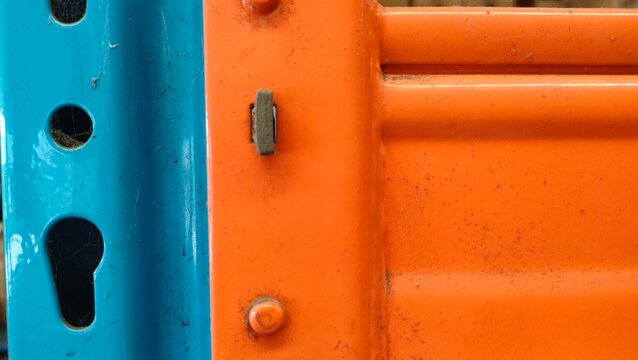 Close-up of a vibrant blue and orange industrial warehouse rack joint. Concept of logistics, storage infrastructure, warehouse management, modular shelving systems, and professional industrial hardwar