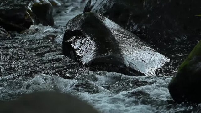 Cinematic slow-motion style of clean river stream rushing through black stones in a forest.