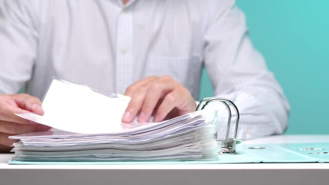 Person's hands organizing numerous paper documents within an open ring binder, representing tasks related to archiving, bookkeeping, data management, and business administration