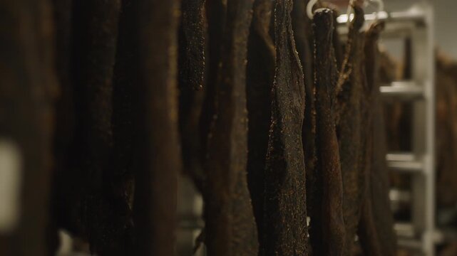 Rows of dark dry beef pieces hang from a metal rail in a biltong curing facility with shallow depth of field.