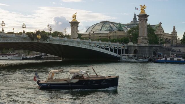 A private luxury motorboat cruises on the Seine River past the historic Alexandre III bridge and Grand Palais dome in Paris France. Premium European travel charter and lifestyle vacation.