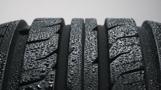 Water Drops on a New Car Tire. Wet tire spinning on a white background close-up. It is covered with sparkling water drops