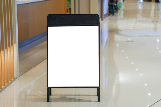 Blank white indoor advertising stand sandwich board mock up template. Clear street signage board placed by an indoors dinning area of a restaurant in shopping mall.