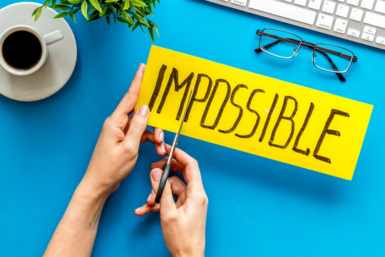 All is possible concept. Hands cut word impossible on blue office desk