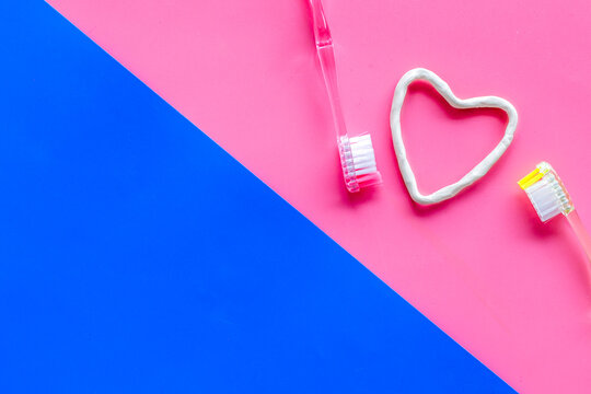 Teeth care. Heart drawn with toothpaste near toothbrushes on pink and blue background top view copy space