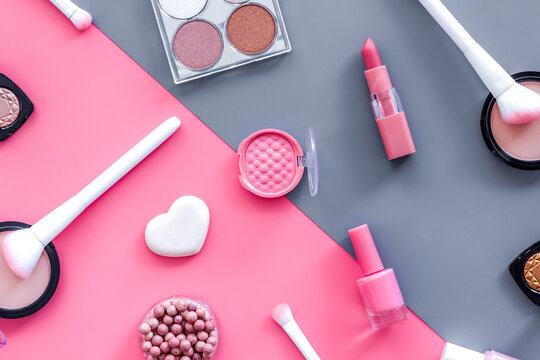 Makeup background with rounge, powder and tools on pink and grey table top view