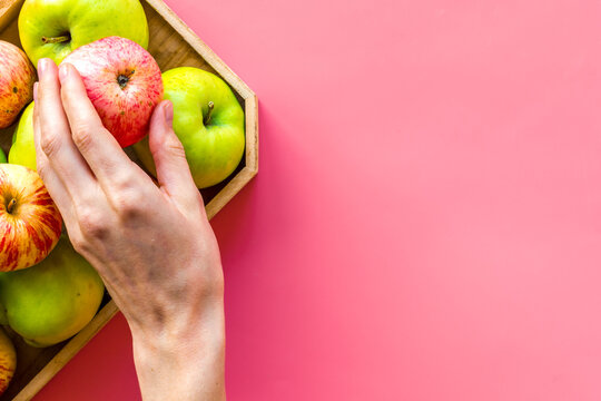 Healthy diet concept. Fresh apples in tray, hand hold apple, pink background top view copy space
