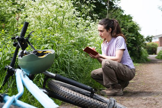 Young environmentalist with book examining plants crouching on road