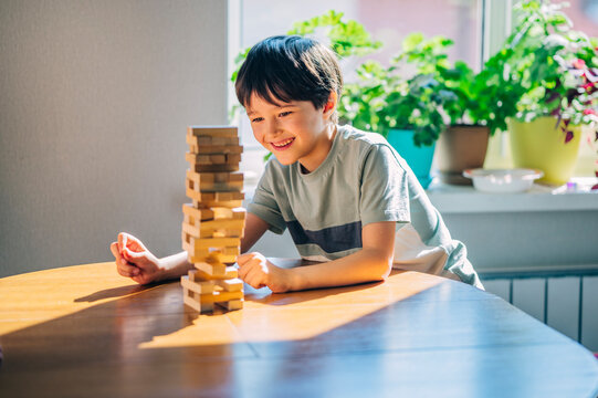Smiling child playing with wooden block tower at home in sunlight