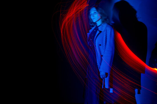 Woman stands in dark room with red and blue light painting