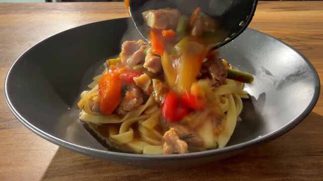 Pouring hot meat gravy with vegetables over freshly cooked noodles in bowl &ndash; laghman style

