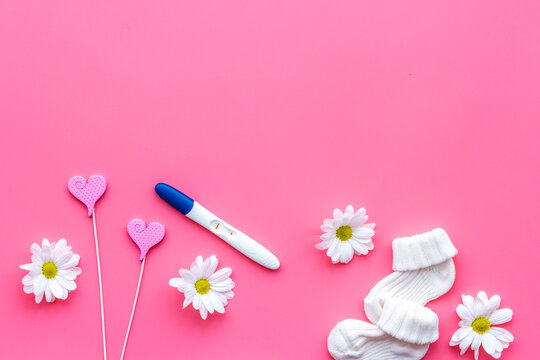 Pregnancy test, socks and flowers pink background top view mock up