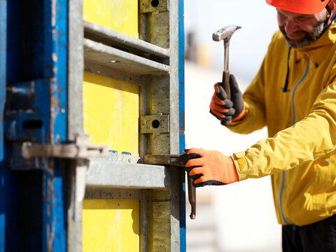 Worker hammering nail on formwork wall at construction site