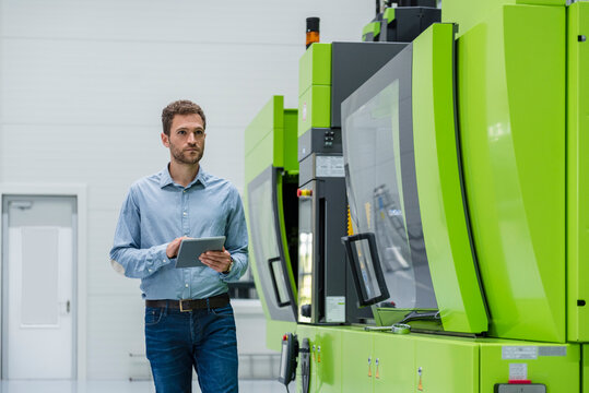 Businessman in high tech company controlling manufacturing machines, using digital tablet