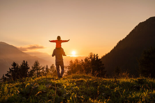 Man carrying daughter with arms outstretched walking at mountain