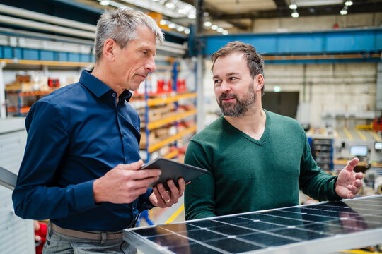 Manager explaining solar panel to businessman at factory