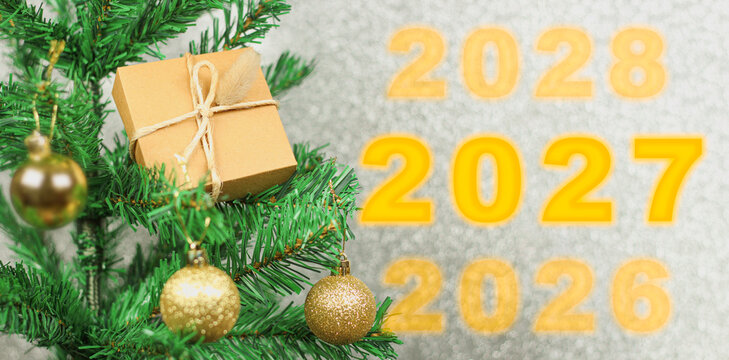 Happy New Year 2027 anniversary. Transition from 2026 to new year 2027 concept image with golden ball ornament on Christmas tree.
