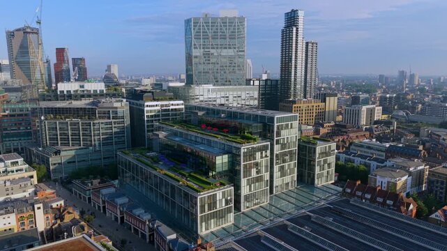 Aerial video looking featuring modern corporate office complexes with green rooftop terraces and glass facades near Spitalfields, London at sunrise.