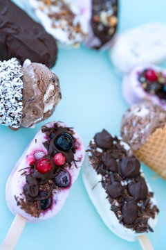 Colorful assortment of homemade yogurt popsicles. Vanilla and chocolate decorated with nuts and frozen berries on ice blue background. Perfect for summer party. Vertical top view close-up with short d