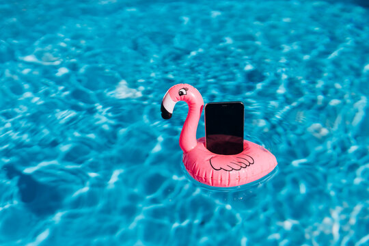 Smartphone on pink flamingo float in swimming pool