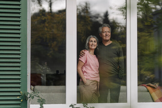 Senior couple behind windowpane of their home looking out
