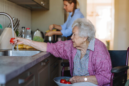 Senior woman washing tomatoes with home caregiver working in background