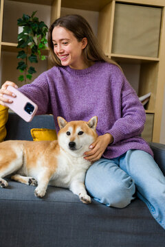 Smiling woman taking selfie with dog on sofa at home